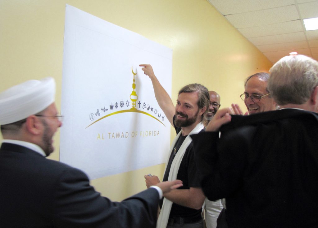 Imam Zaher Badaraany, Rev. Chris Miller, and Ted Brownstein work together to name all of the religions represented on the banner